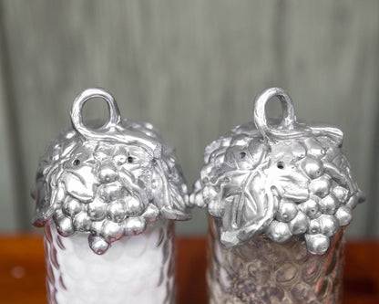 "Grape Salt and Pepper Set"Add a touch of sophistication to your table with this Grape Salt and Pepper Set from Arthur Court. The top of these dispensers features a looping vine adorned with leaves and grapes, creating a unique and elegant design. Handcrafted from aluminum, these pieces will elevate any setting with their simple yet luxurious appearance. Measuring at a diameter of 2.0" and a height of 5.75", these easily refillable dispensers can be dusted with a damp cloth and will not tarnish over time"